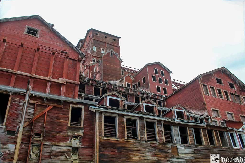 Front of the Concentration Mill Kennecott Mine: A complex of weathered, red wooden buildings with varying roof shapes, showing signs of decay and disuse.