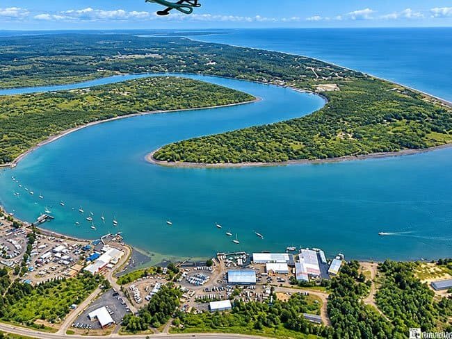 Aerial view of a riverbend entering the sea with a town in the foreground.