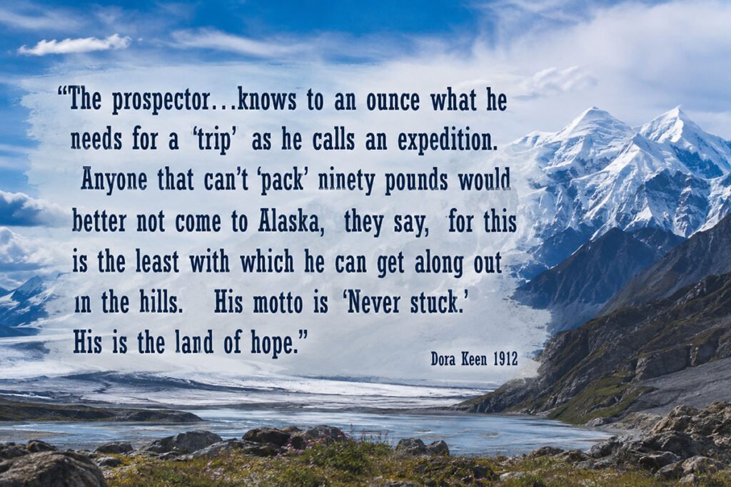 A stunning Alaskan landscape featuring snow-capped mountains, a glacial river, and rocky terrain, with a historical quote about prospectors in Alaska overlayed on the image.
Transcribed Text:
"The prospector...knows to an ounce what he needs for a 'trip' as he calls an expedition. Anyone that can't 'pack' ninety pounds would better not come to Alaska, they say, for this is the least with which he can get along out in the hills. His motto is 'Never stuck.' His is the land of hope."
Dora Keen 1912