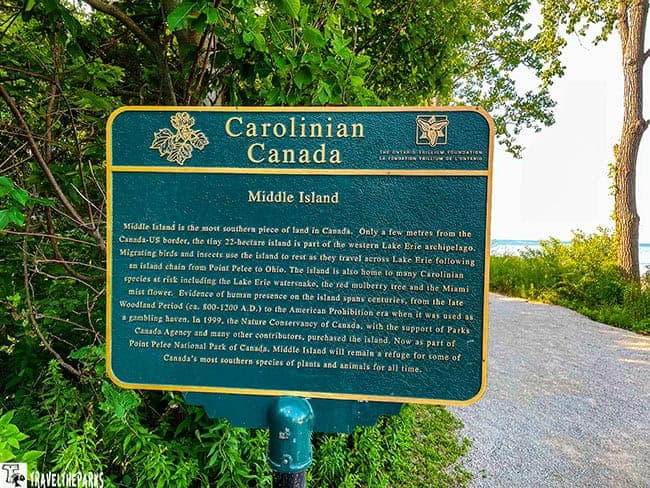 Informational sign about Middle Island at Point Pelee National Park, surrounded by trees and a gravel path.