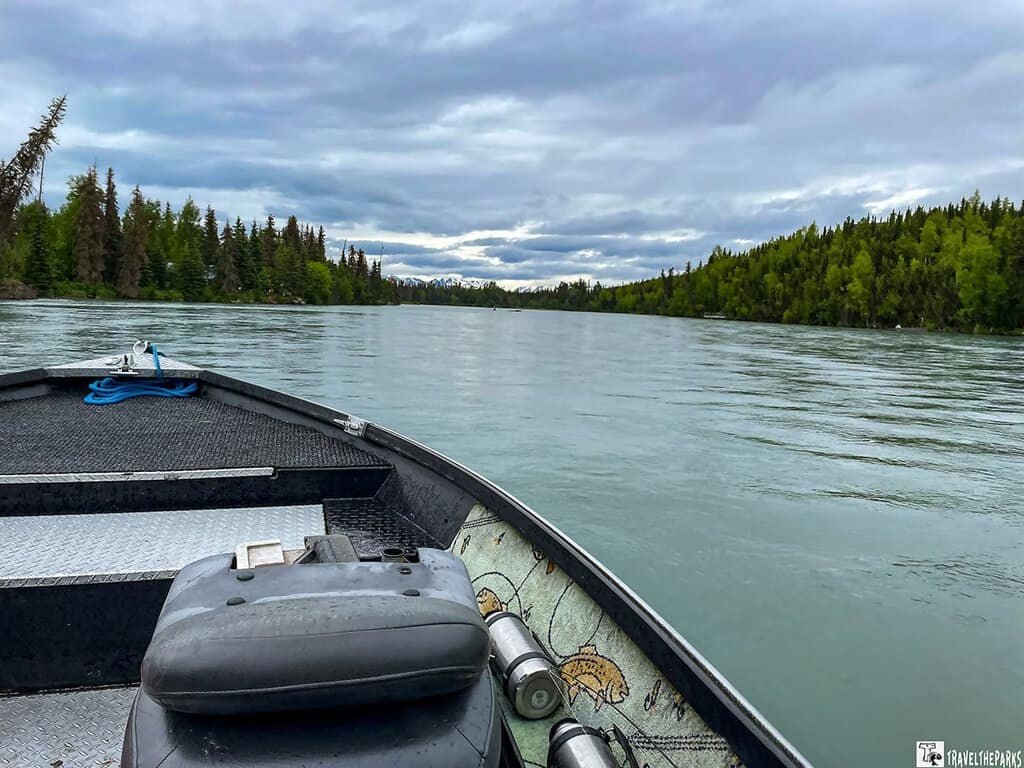 A view from inside a boat on a calm Kenia river surrounded by trees under a cloudy sky.