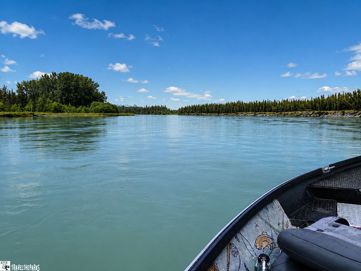 A boat on a turquoise river with mountains and a forest in the background in Alaska.