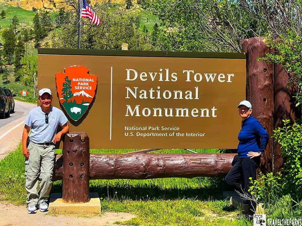 Two people posing next to the Devils Tower National Monument sign.