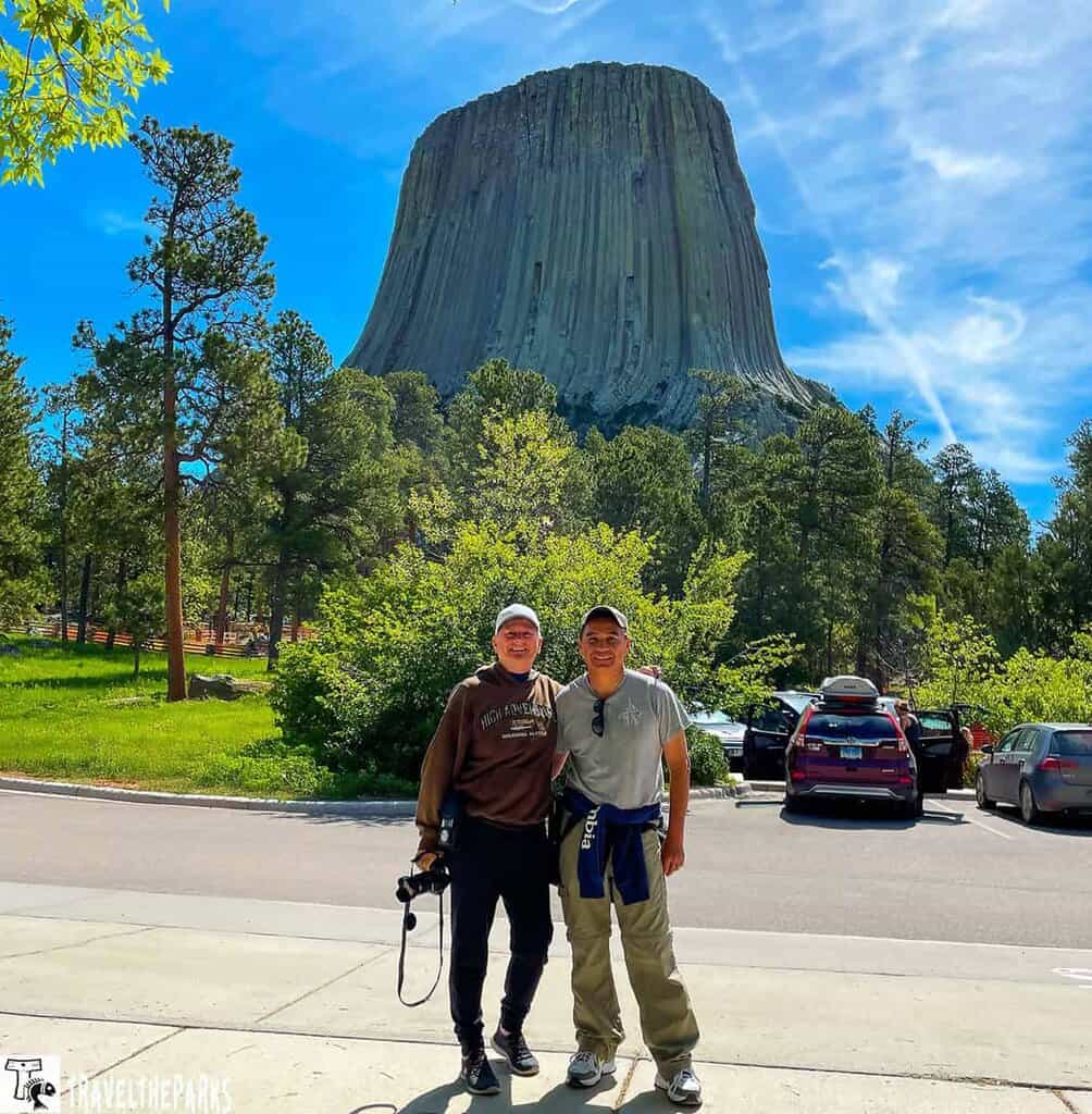 Two people standing in front of Devils Tower with a clear blue sky.