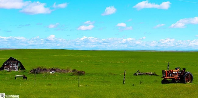 A green field with a partially collapsed barn and an old tractor under a blue sky.