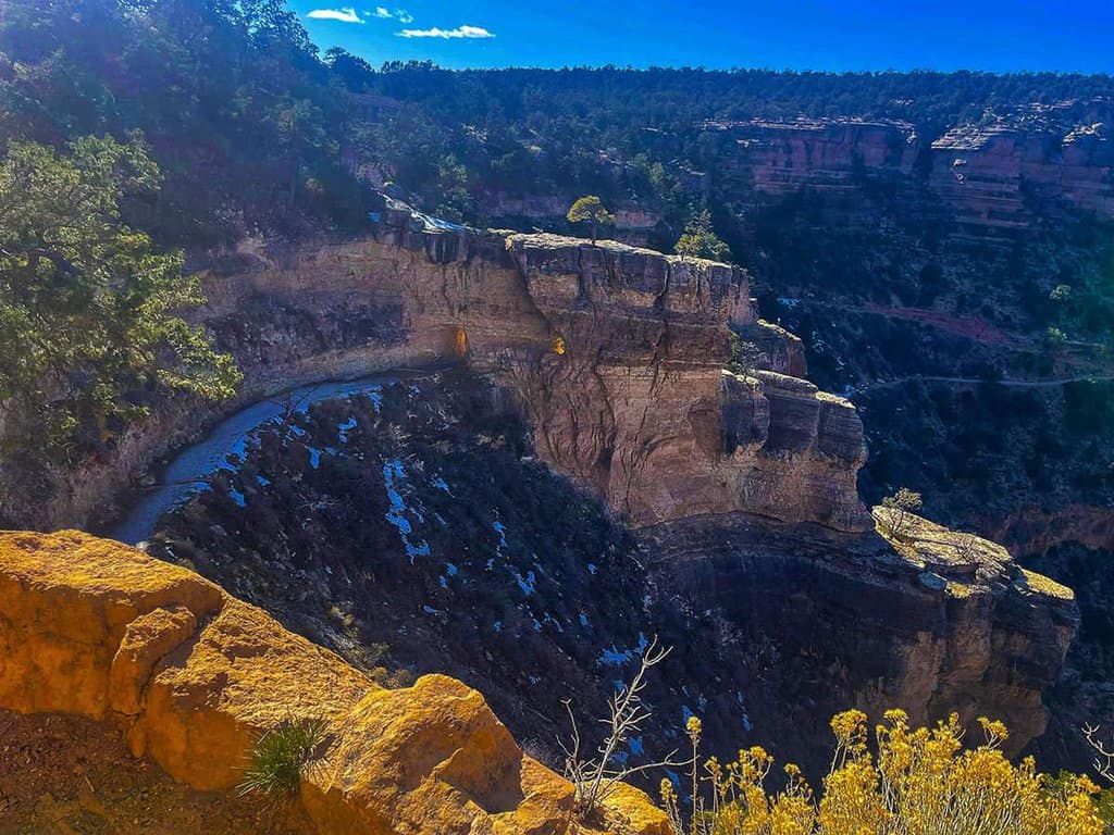 View of the Grand Canyon with rocky cliffs, a winding path, and a blue sky.