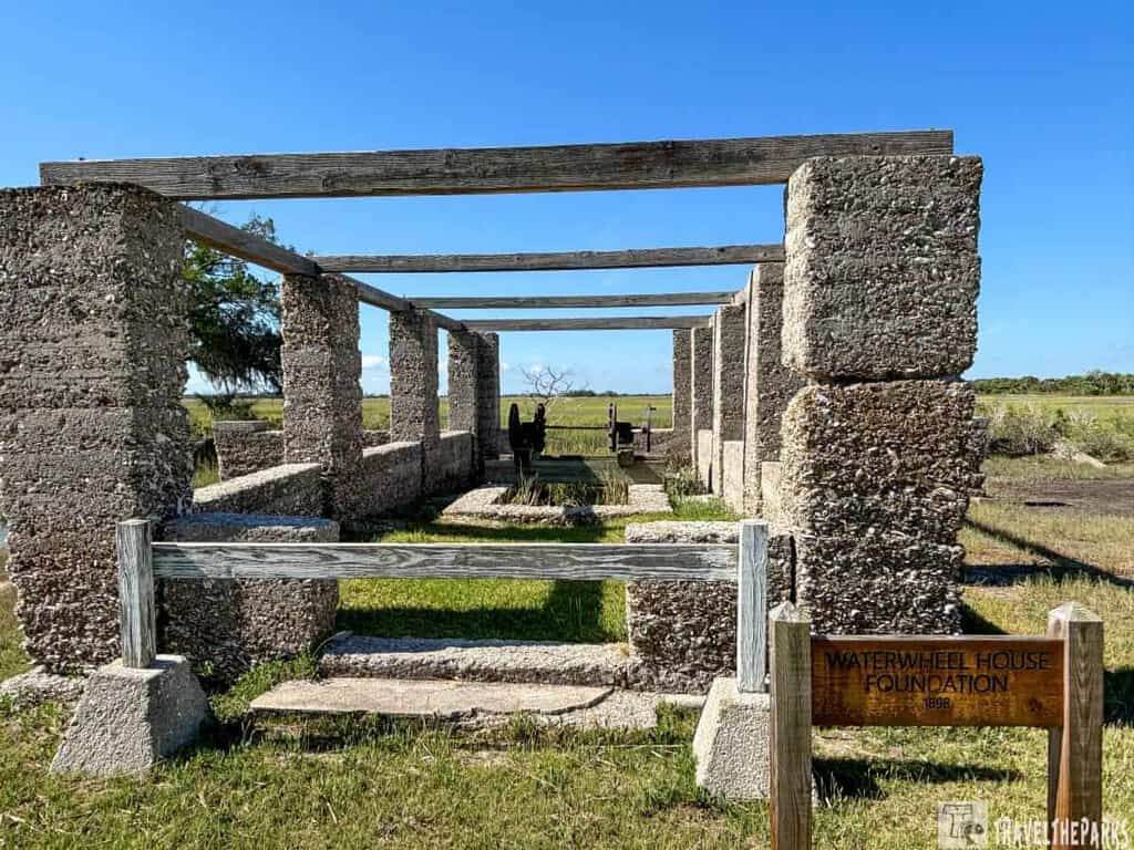 Dungeness Ruins of the Waterwheel House Foundation with stone columns and wooden beams set in a grassy field.