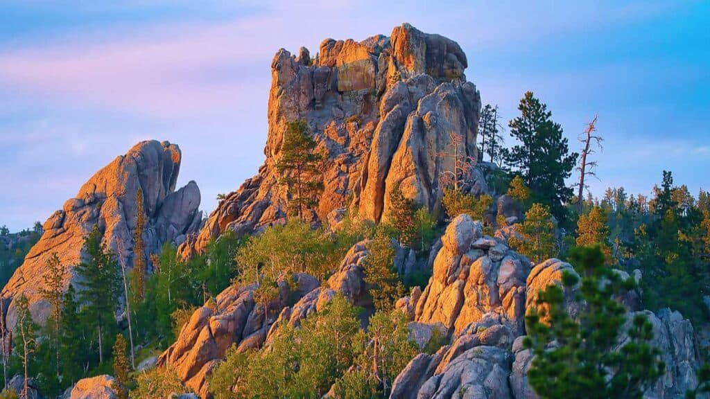 A large rock formation with trees and a sky in blue and pink hues.