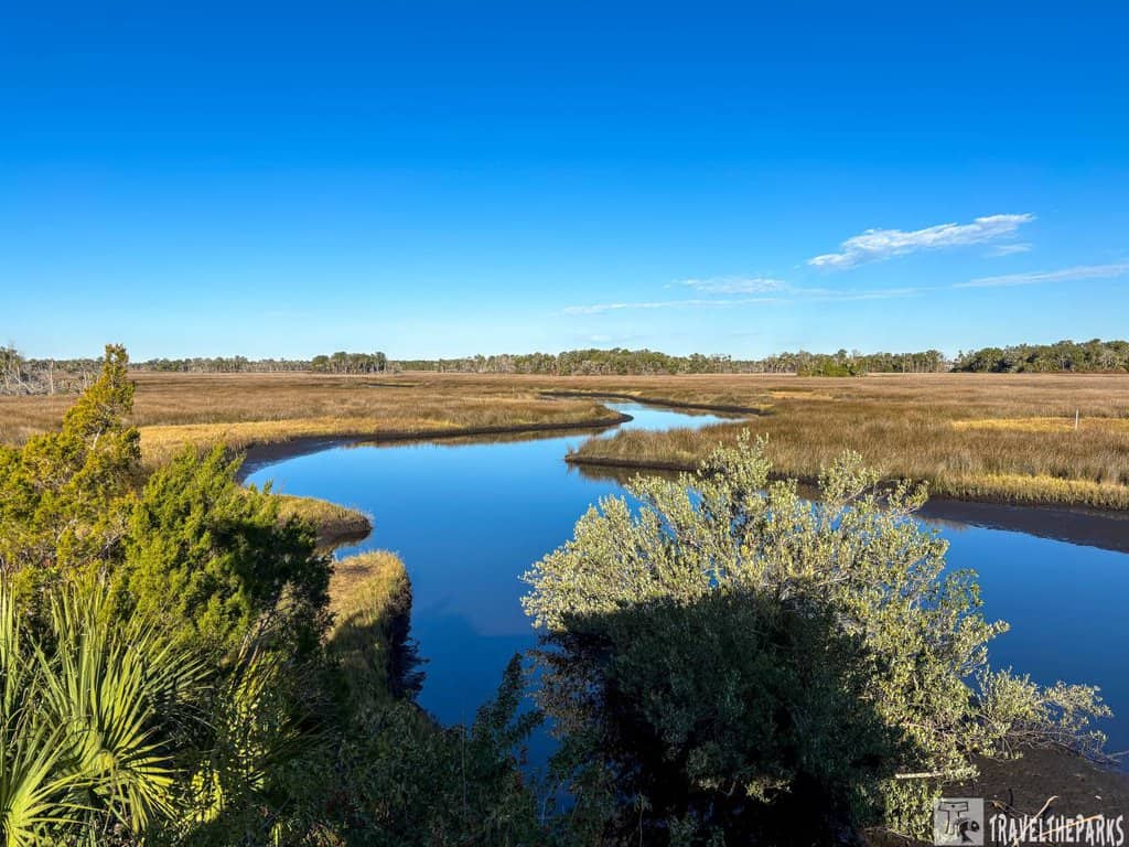 A scenic view of a river winding through the grassy landscape of Chassahowitzka National Wildlife Refuge under a clear blue sky.