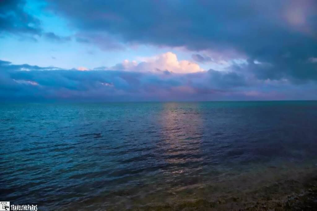 A Florida Nature Coast seascape with dark clouds overhead and sunlight illuminating patches of the ocean and clouds.
