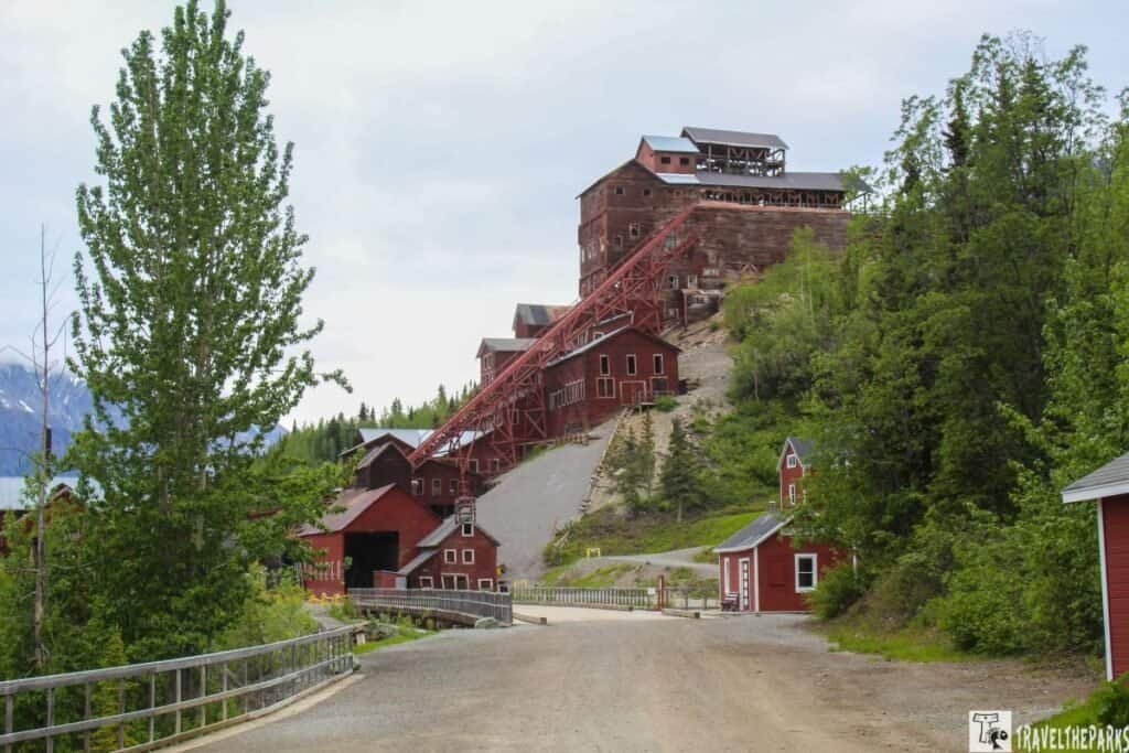 View of the Kennecott mine with red buildings and a conveyor belt on a mountain slope under an overcast sky.