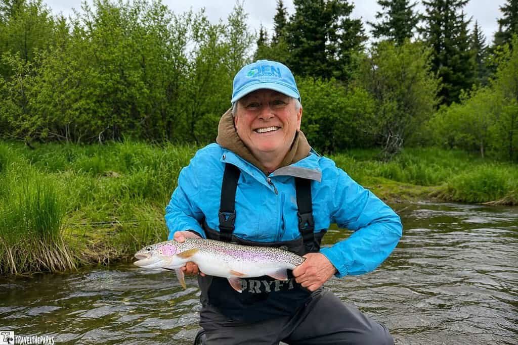 A woman in a blue jacket holds a giant rainbow from the Brooks River