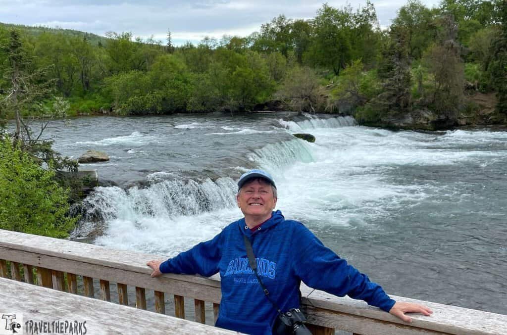 A person stands at Brooks Falls Viewing Platform with Brooks falls in background