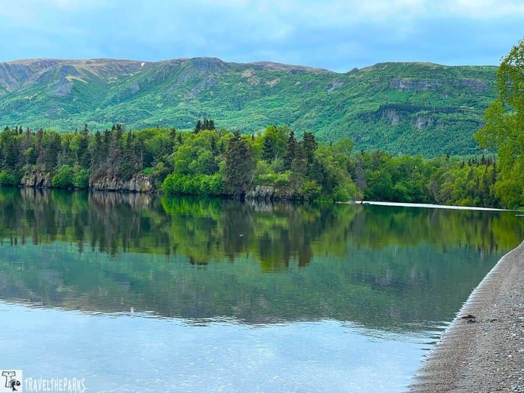 A calm Brooks Lake with Dumpling Mountain in the background. The trees and mountain are reflected int he lake.