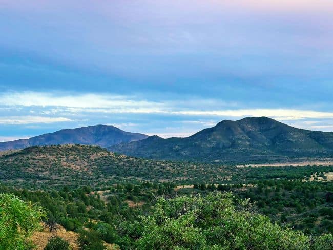 View of the Davis Mountains with lush greenery, rolling hills, and prominent mountain peaks under a colorful sky.