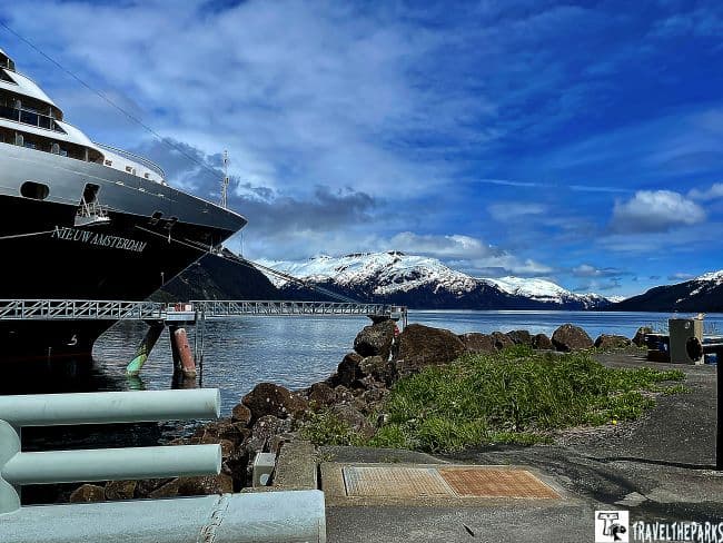 A large ship docked near a whitter alaska pier with snow-capped mountains in the background.