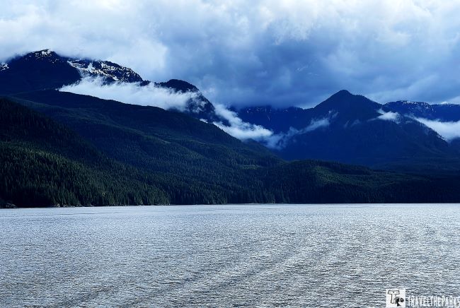Serene landscape of the inside passage with misty, forested mountains and overcast sky.