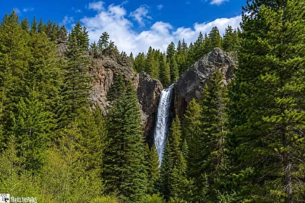 Treasure Falls View-Colorado: Waterfall flowing down a rocky cliff surrounded by a dense green forest.