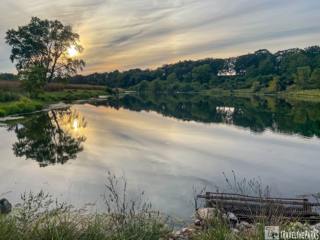 Sunset over a reflective river with trees and grasses.