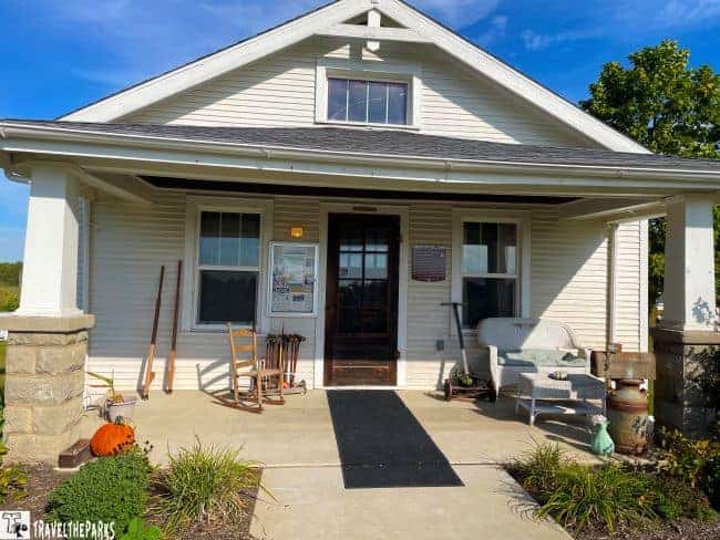 Front view of a white, single-story building with a porch, chairs, and a pumpkin on a concrete path.