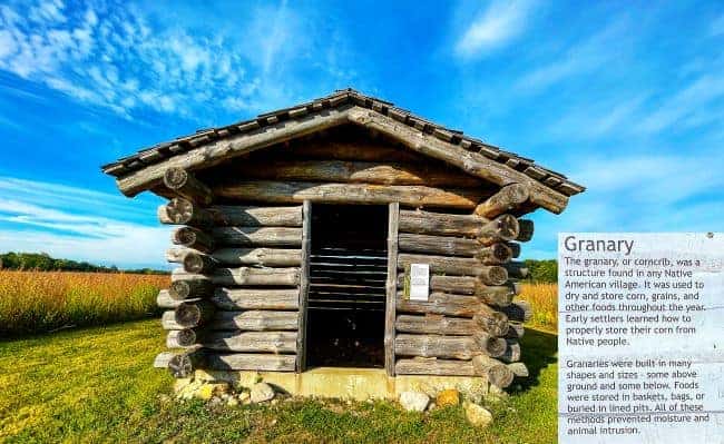 Prophetstown State Park historic site log granary in a grassy field under a blue sky, with accompanying text on the right.