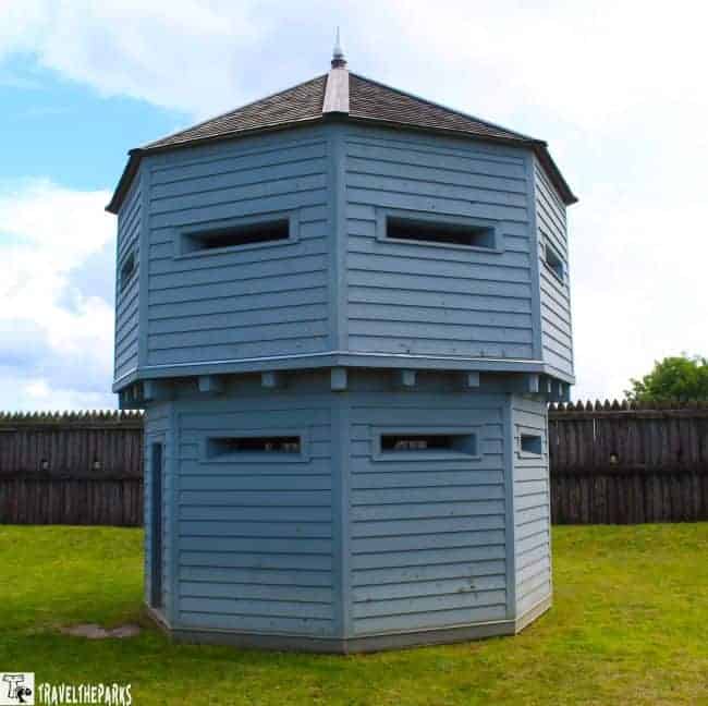 Light blue octagonal guard tower with narrow windows, surrounded by a wooden fence and grassy area.