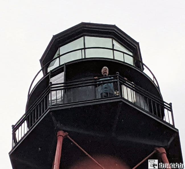 Crooked River Lighthouse: Upward view of a lighthouse with a person at the railing, against an overcast sky.