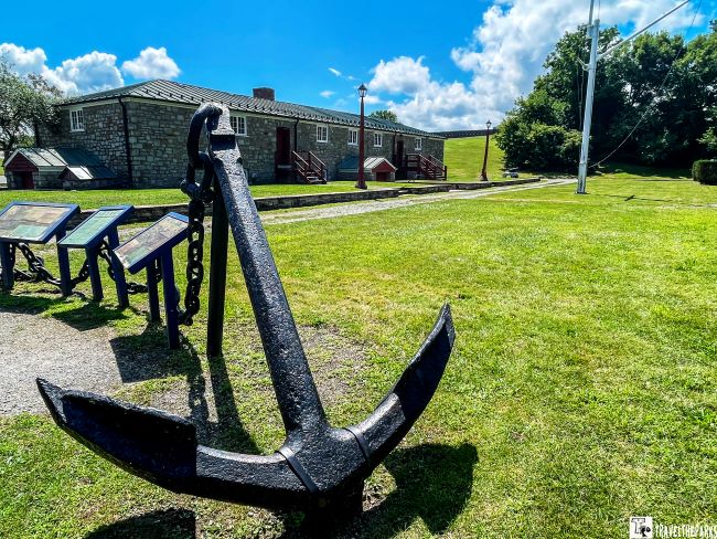 Large black anchor on a grassy field with the stone Navy Yard building and information stands in the background.