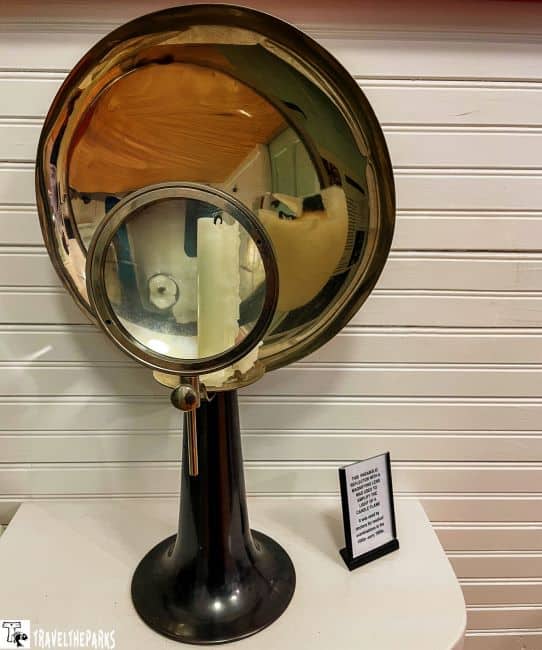 A parabolic reflector with a smaller mirror on a metallic stand, next to a light switch.