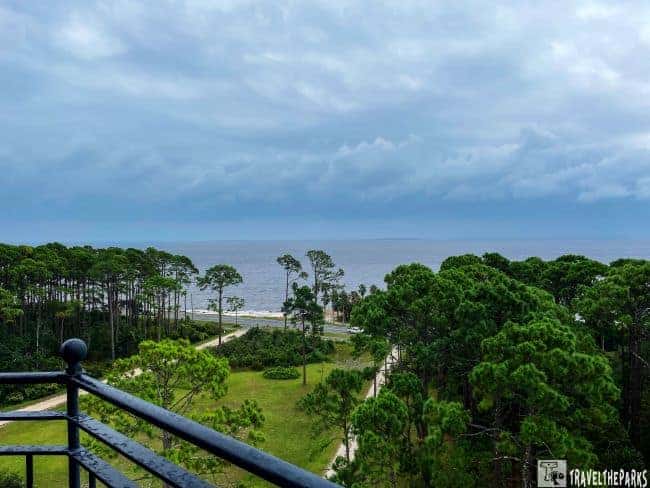 Top of the Crooked River Lighthouse view of a coastal landscape with pine trees, a path, and the sea under an overcast sky.