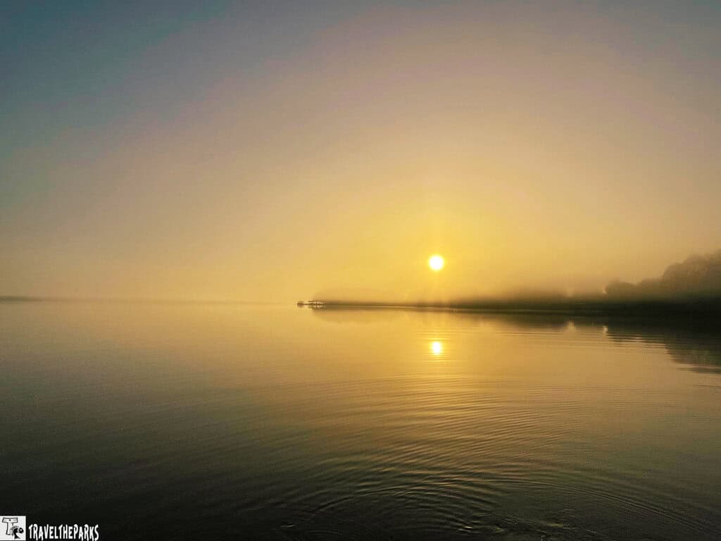 Sunrise over a tranquil Indian River lagoon with sun reflection and faint tree silhouettes.