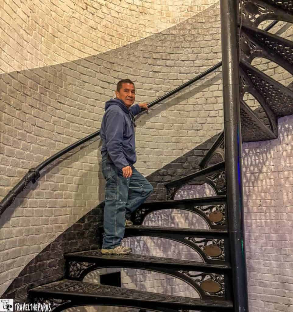 Man climbing a spiral metal staircase inside a brick structure.