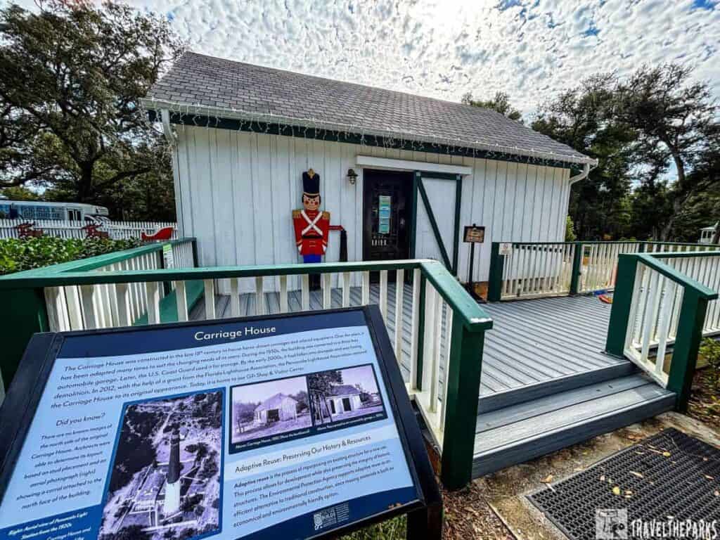 White building with a gray roof, marked as the Carriage House, with a deck and information panel in the foreground.