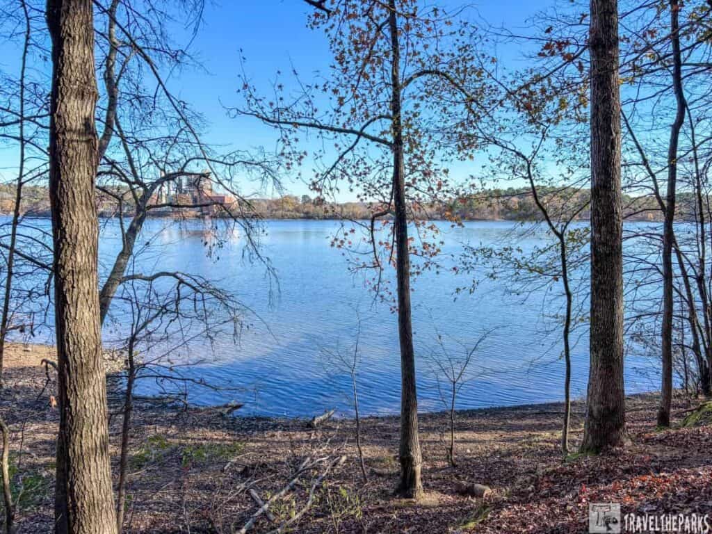 View of a lake through trees of the Power Plant in Lake Catherine State Park, with a clear sky and autumn foliage.