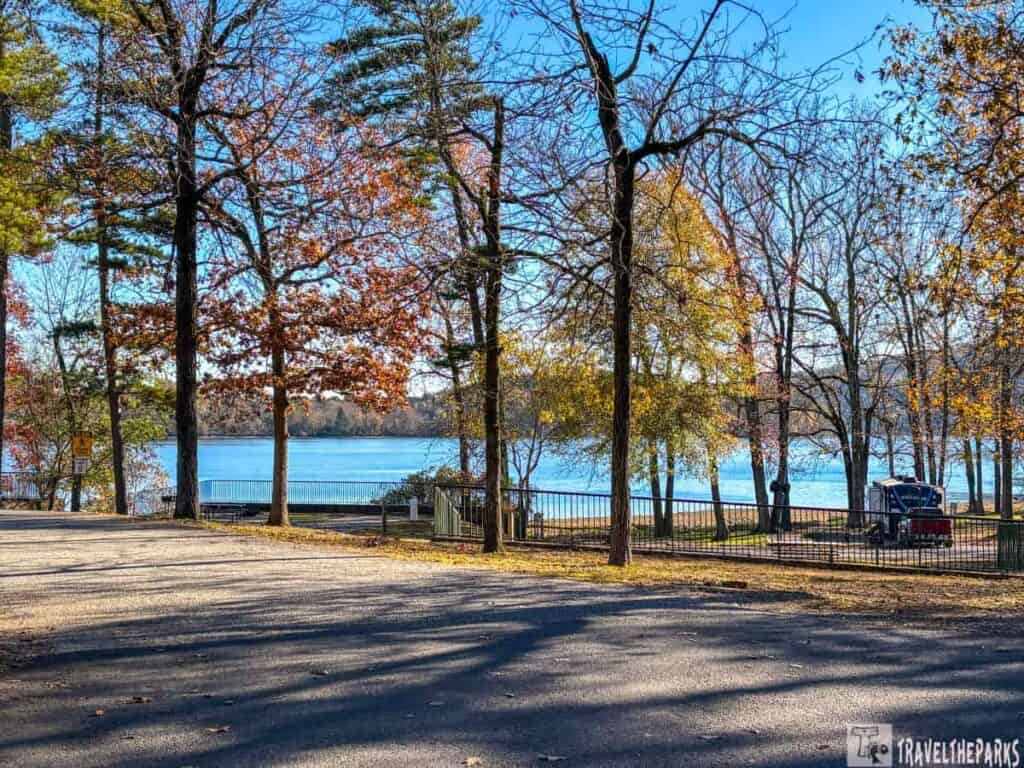 Autumn scene at Lake Catherine State Park with trees, a calm lake, and a parked vehicle with a camping trailer.