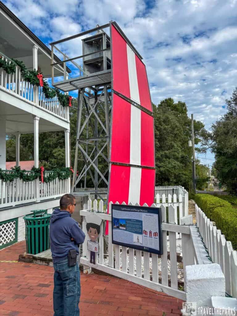 A man observes an educational display in front of a red and white range marker, with a festive porch nearby.