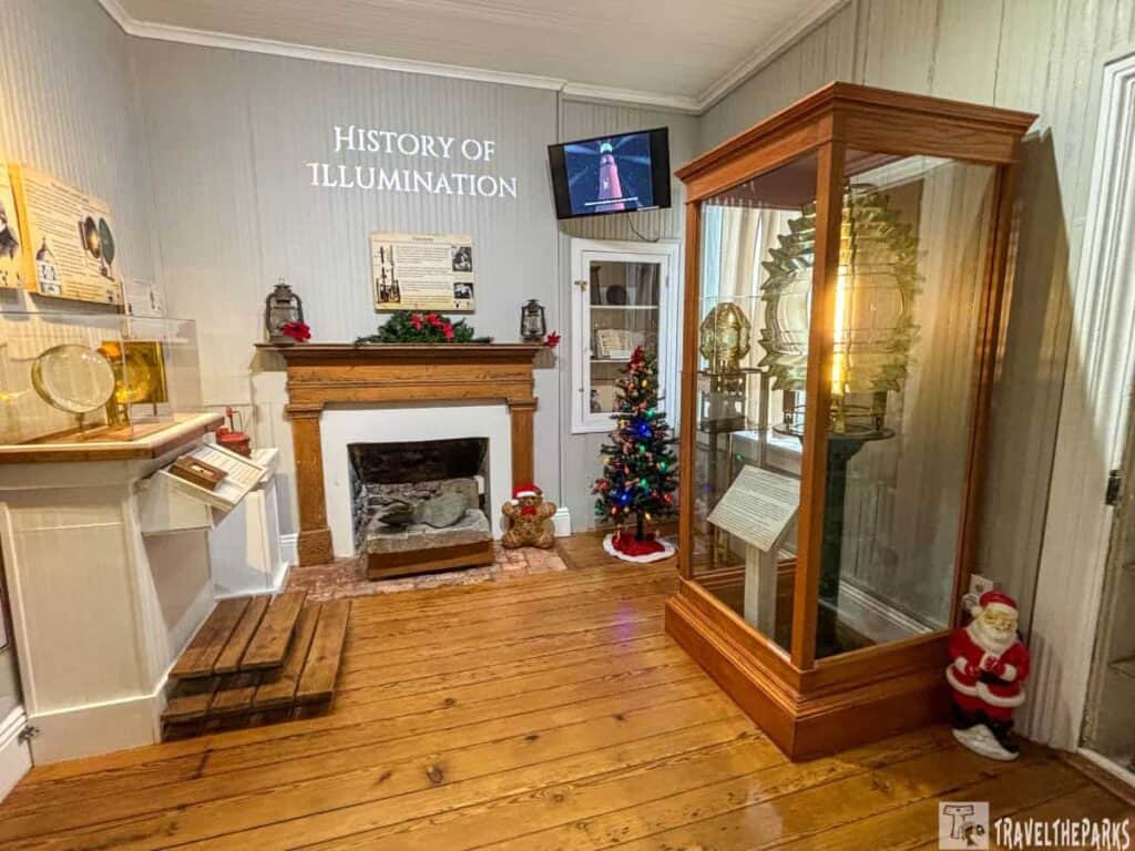 Museum room showcasing the history of lighthouse illumination, with wooden floors, a decorated Christmas tree, and a large Fresnel lens display.