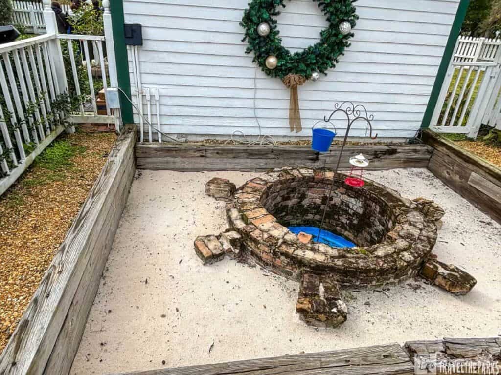 Circular brick well with a wreath on a white building wall in the background.