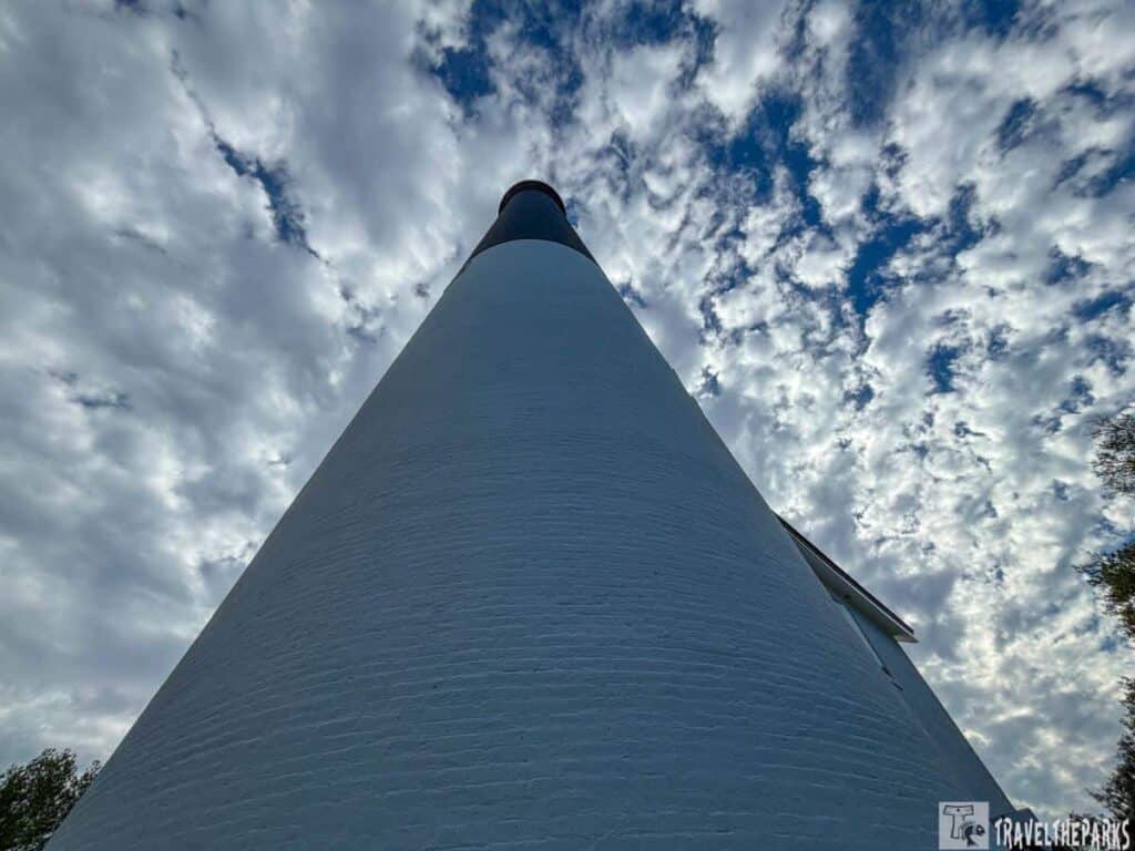 Low-angle view of the white Pensacola Lighthouse against a partly cloudy sky.