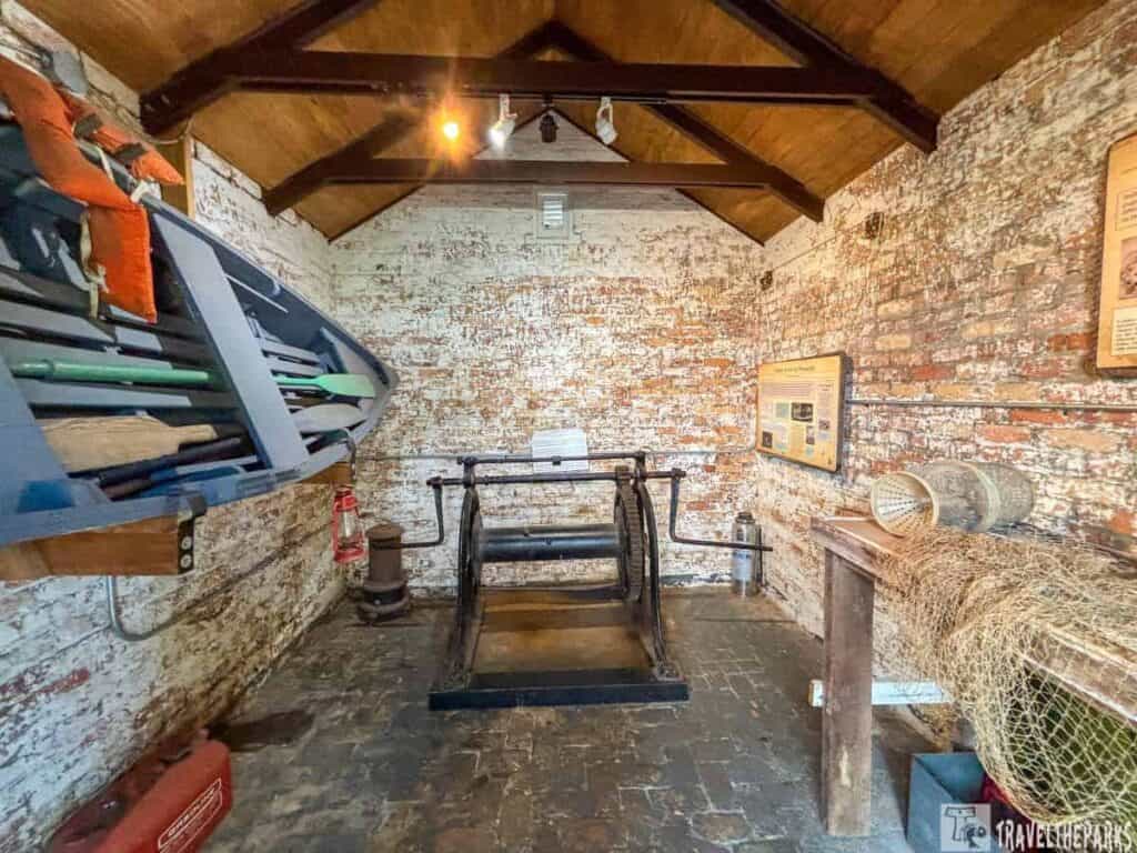 Interior of a historic Oil House room with a mounted lifeboat, fishing nets, and a large metal mechanism.