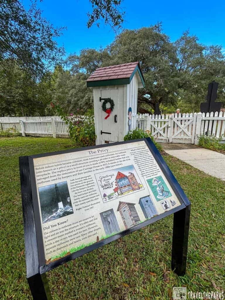 Historical privy display at Pensacola Lighthouse with a sign and a small outhouse behind it.