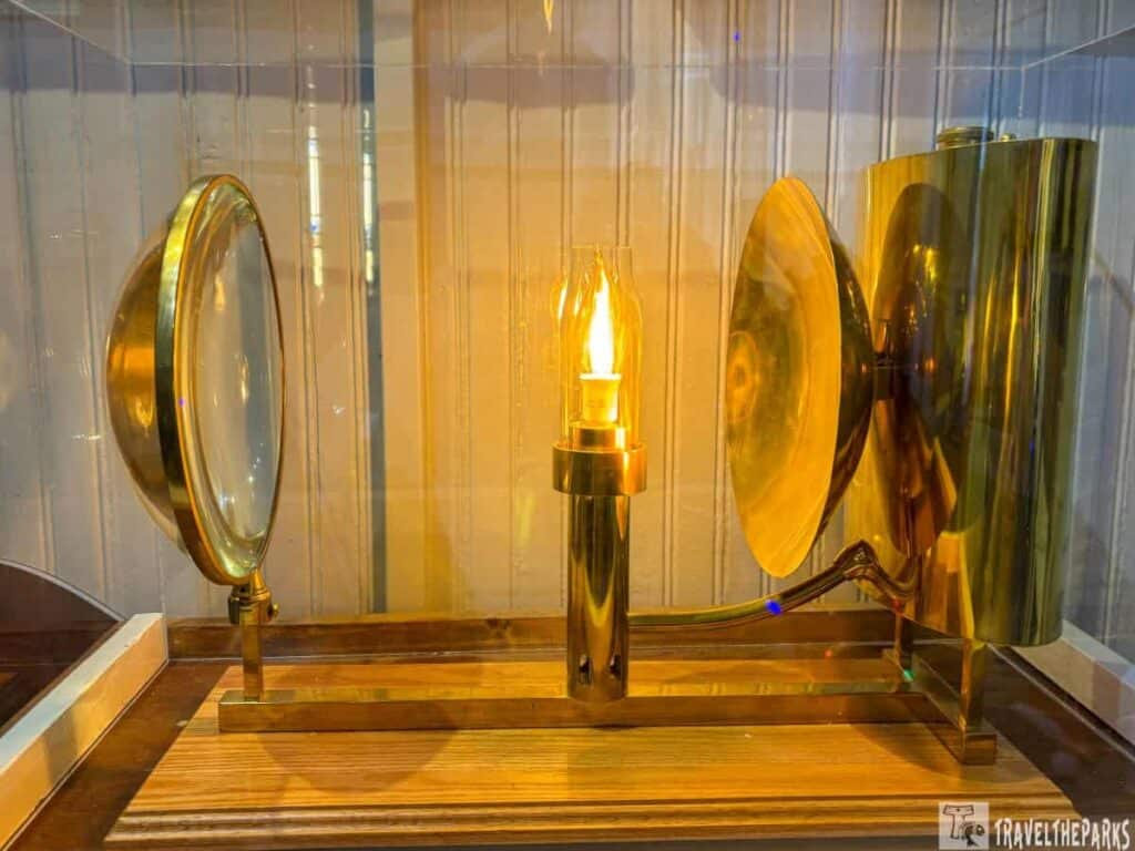 Winslow Lewis lighthouse lamp with a flame, lens, and brass reflector in a display case.