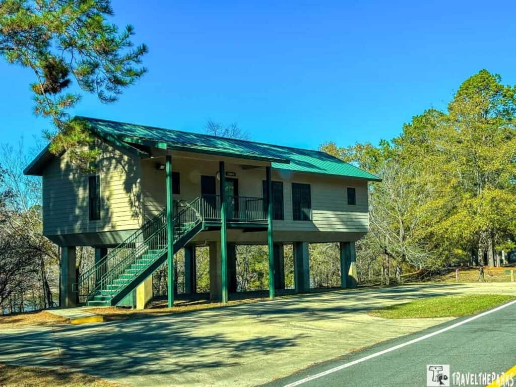 Elevated building on stilts with green roof in a wooded area.