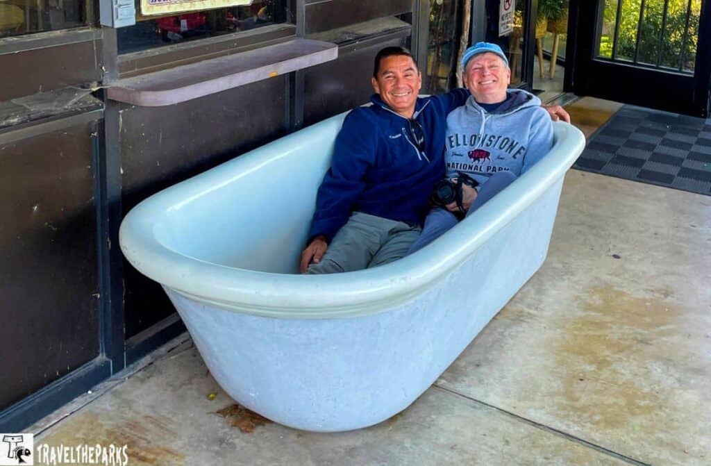 Two people sitting in a white bathtub outdoors, smiling.