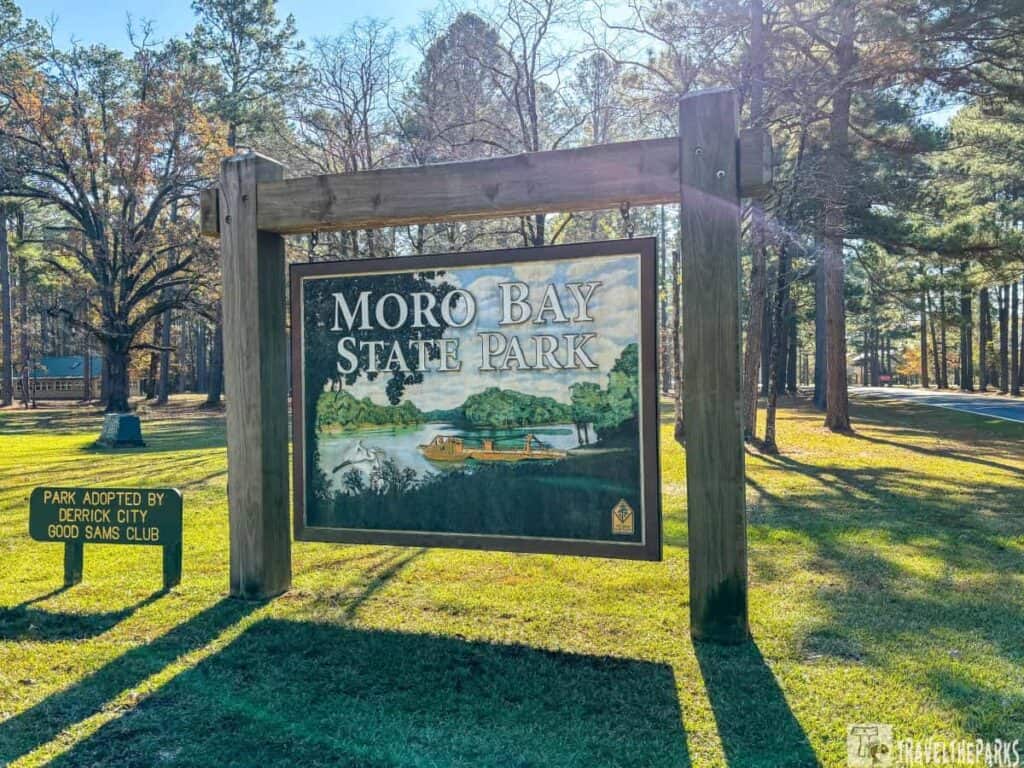 Sign for Moro Bay State Park with a painted nature scene, surrounded by trees.