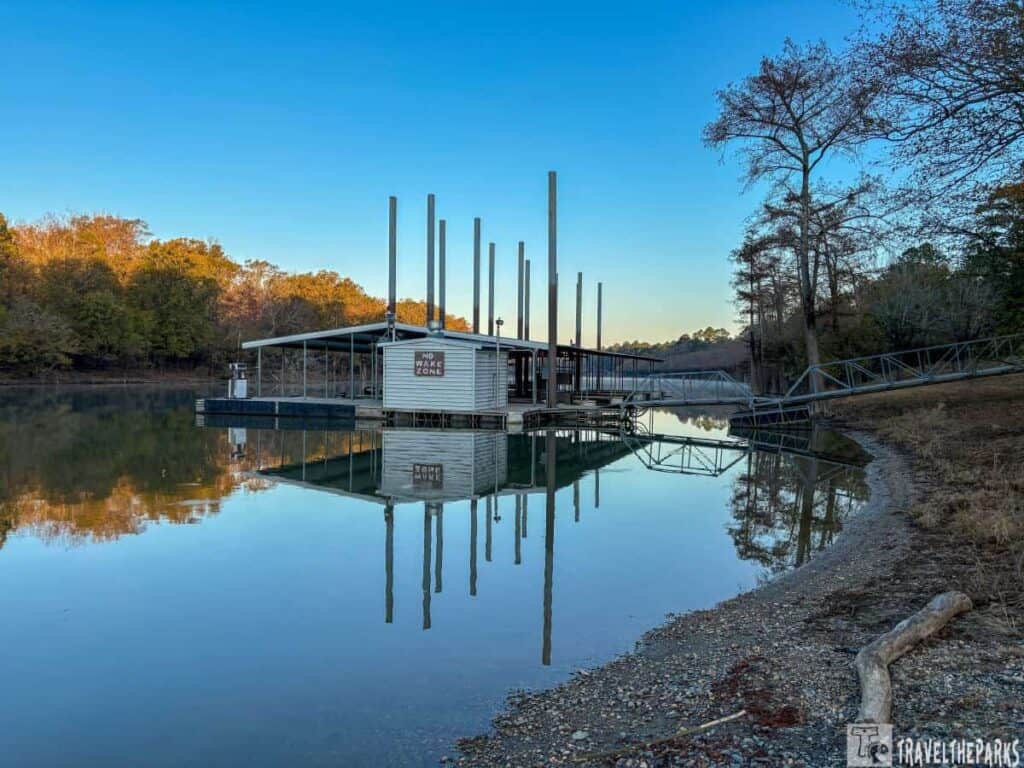 Dock with a "NO WAKE ZONE" sign on calm water, surrounded by trees under a clear blue sky at Moro Bay State Park.