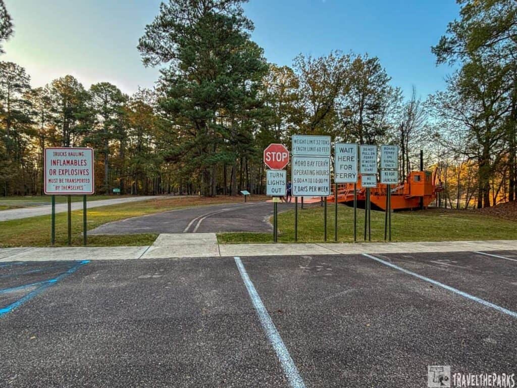Parking lot with signs and an orange ferry structure surrounded by trees.