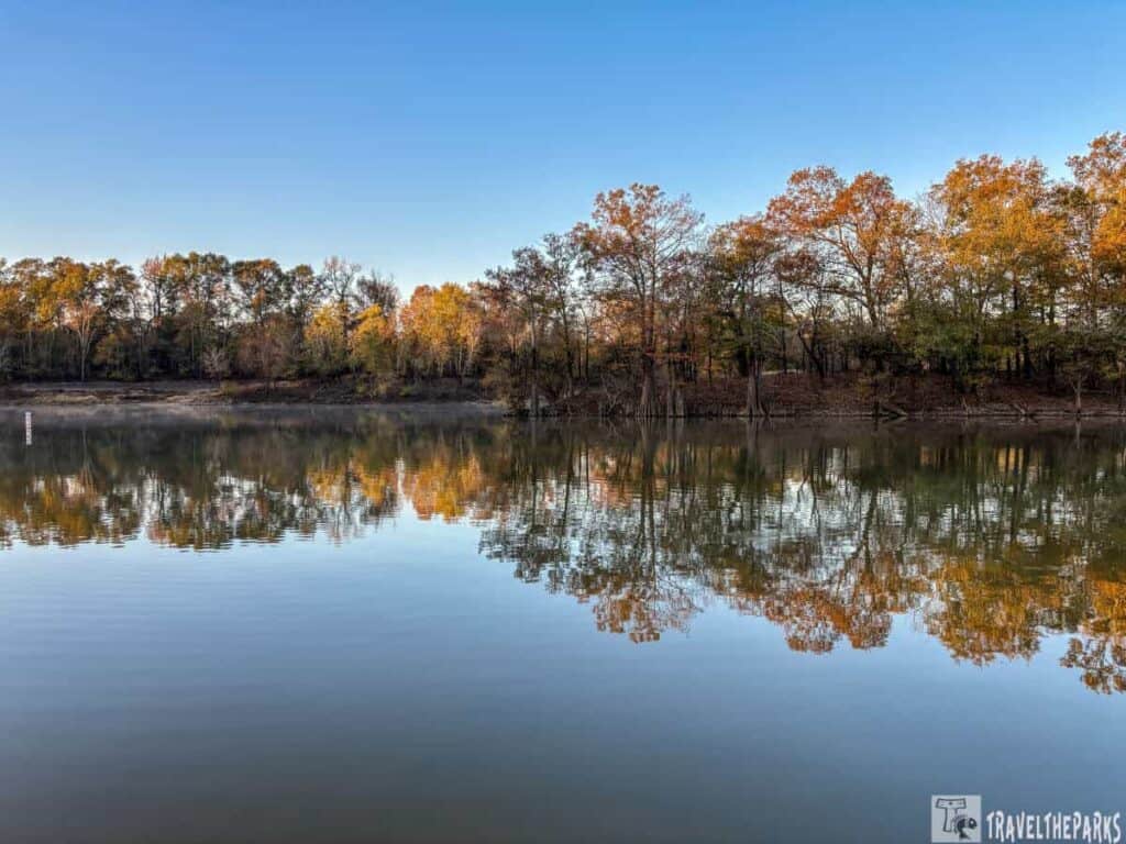 Calm water reflecting autumn trees at Moro Bay State Park under a clear blue sky.