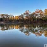 Calm water reflecting autumn trees at Moro Bay State Park under a clear blue sky.