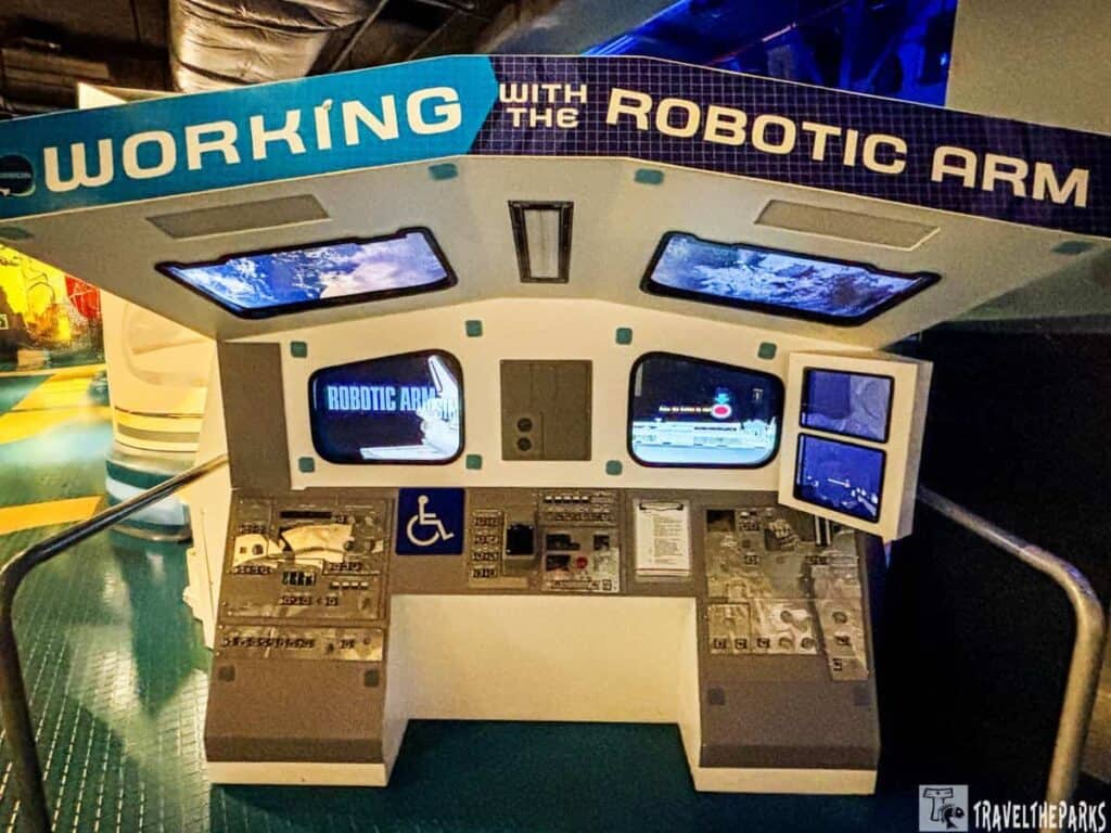 Control console for a robotic arm exhibit with screens and interactive controls.